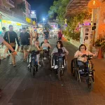 A group of wheelchair users with motorized adaption cruise Thailand at night.